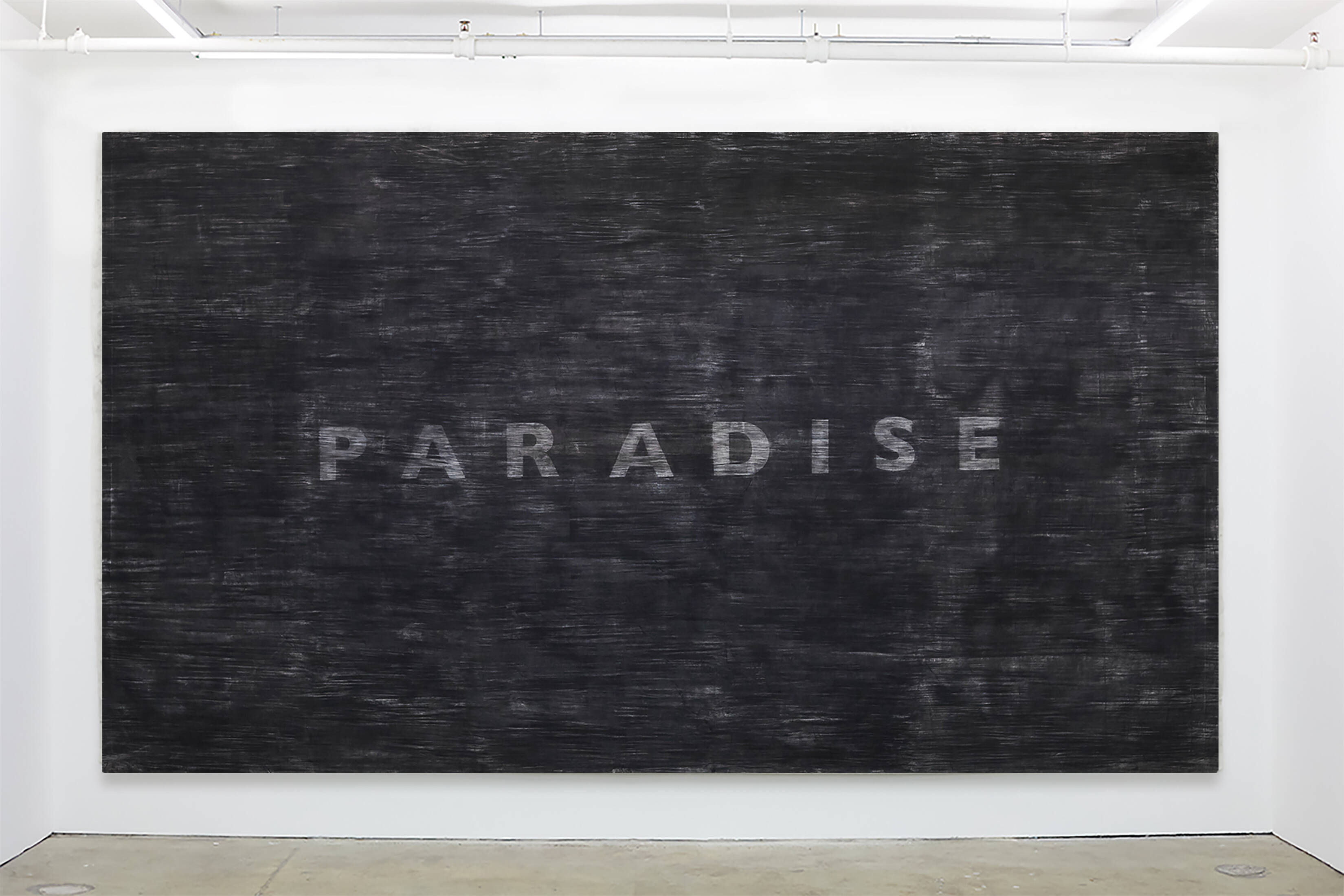 Carbon residue on muslin shows the word “paradise” in gray capital letters against a black background.